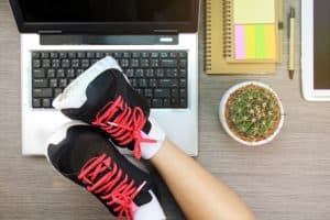 Image of a person with running shoes on with their feet up on a work desk