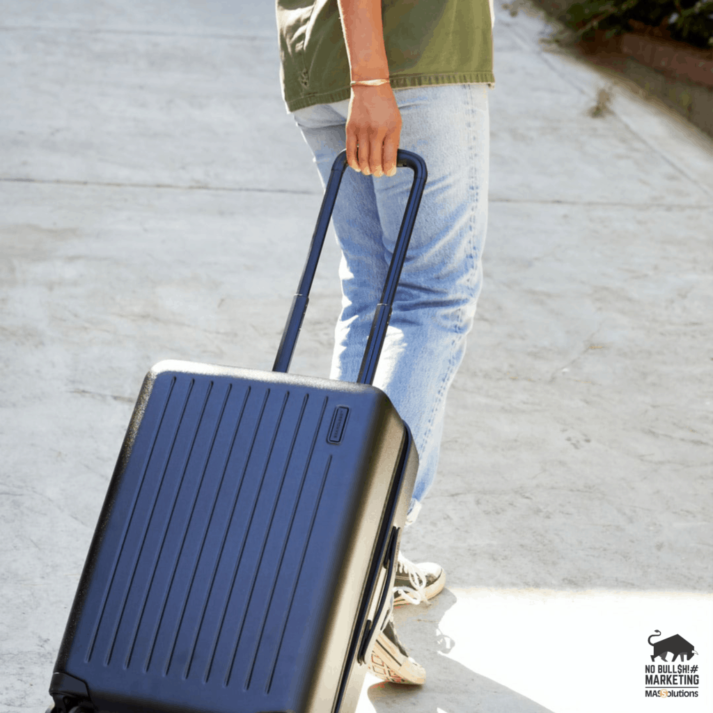 Picture of a woman pulling a black, hard-shell suitcase. The image is being used for a blog titled, "Steph Korey Didn't Step 'Away' For Long"